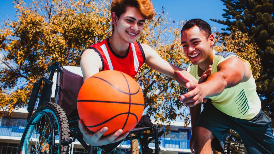 Ein junger Mann im rollstuhl spielt Basketball mit einem jungen Mann ohne Einschränkungen