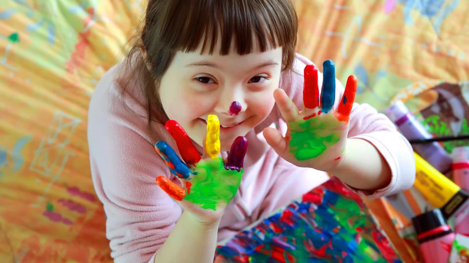 Mädchen mit Downsyndrom hat bunte Farbe an den Fingern