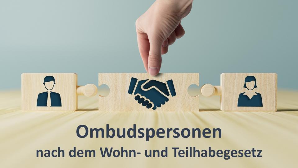 Auf einem Tischplatte aus Holz stehen drei Puzzelstücke aus Holz, die noch nicht ineinandergreifen. Auf dem Puzzleteil links ist ein Mann und auf dem rechten Puzzleteil eine Frau. In der Mitte sind schüttelnde Hände abgebildet. Darunter steht "Ombudspersonen nach dem Wohn- und Teilhabegesetz".