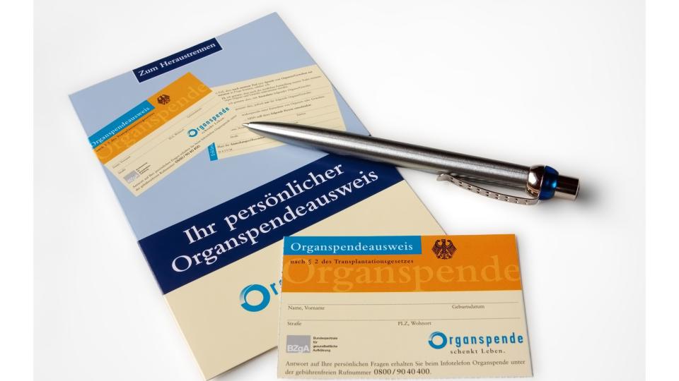 Auf der untersten rechten Ecke einer Broschüre zum Thema Organspendeausweis liegt ein Organspendeausweis. Oberhallb des ausweises liegt ein silberner Kugelschreiber ebenfalls halb auf der Broschüre.