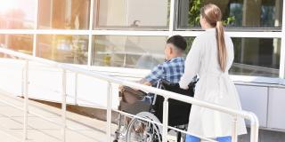 Ärztin schiebt Person im Rollstuhl eine Rampe hinauf