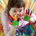 Mädchen mit Downsyndrom hat bunte Farbe an den Fingern