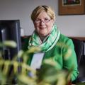 Claudia Middendorf sitzt in ihrem Büro am Schreibtisch am PC und lächelt in die Kamera. Sie trägt eine weiße Bluse, einen grünen Blazer und einen farblich passenden Schal.