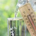 In ein Glas wird Wasser eingeschenkt. Rechts daneben wird ein Thermometer ins Bild gehalten auf dem 40 Grad angezeigt werden. Im Hintergrund sieht man verschwommen Sonnenstrahlen, die durch grüne Bäume scheinen.